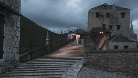 tourists walk over mostar bridge in the evening.