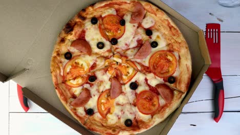 fresh round pizza with tomatoes, sausage, mozzarella and olives in cardboard box rotates slowly.