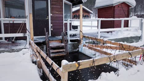 Close-up-of-the-lake-entry-in-a-nordic-sauna-next-to-a-red-wooden-cabin-in-a-frozen-lake-covered-with-snow