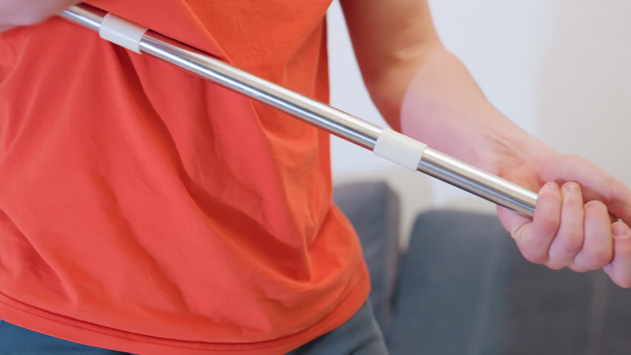 Close up of cleaner in orange shirt holding mop handle playfully like guitar stopping cleaning for fun moment while enjoying chore with creativity before continuing mopping routine