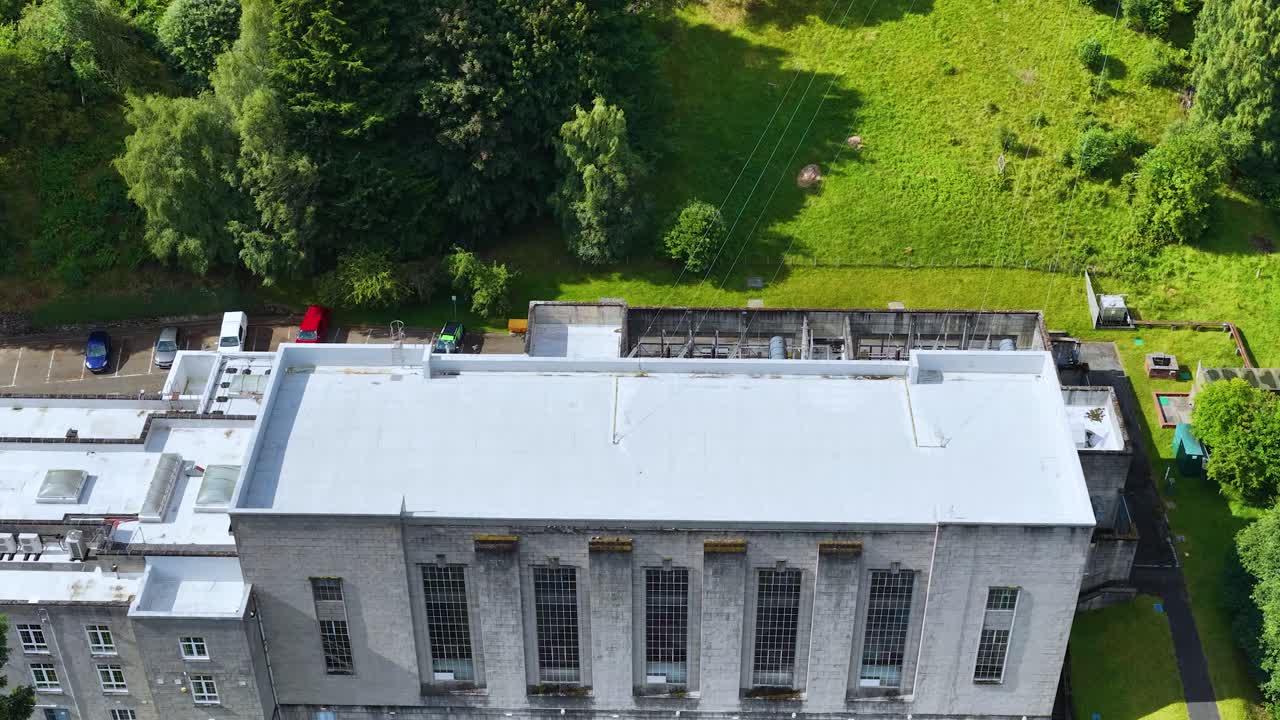 Drone ascends above hydroelectric power station, revealing river, dam, and lush green landscape