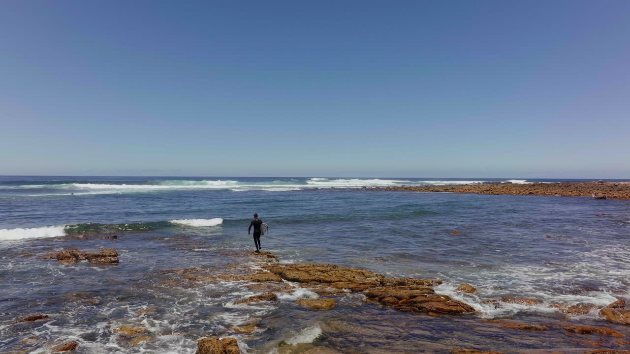 남아프리카 드론 항공 영화 서퍼는 파도를 확인하고 암초 바위 위를  ⁇ 고 서핑 보드를 타기 위해 준비되어 있습니다. 여전히 베이 가든 루트 제프리스 베이 낮낮늦은 아침 여름 서핑 앞으로