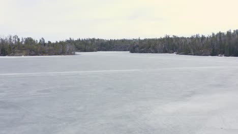 aerial dolly forward over melting frozen lake with ice roads still visible in canada