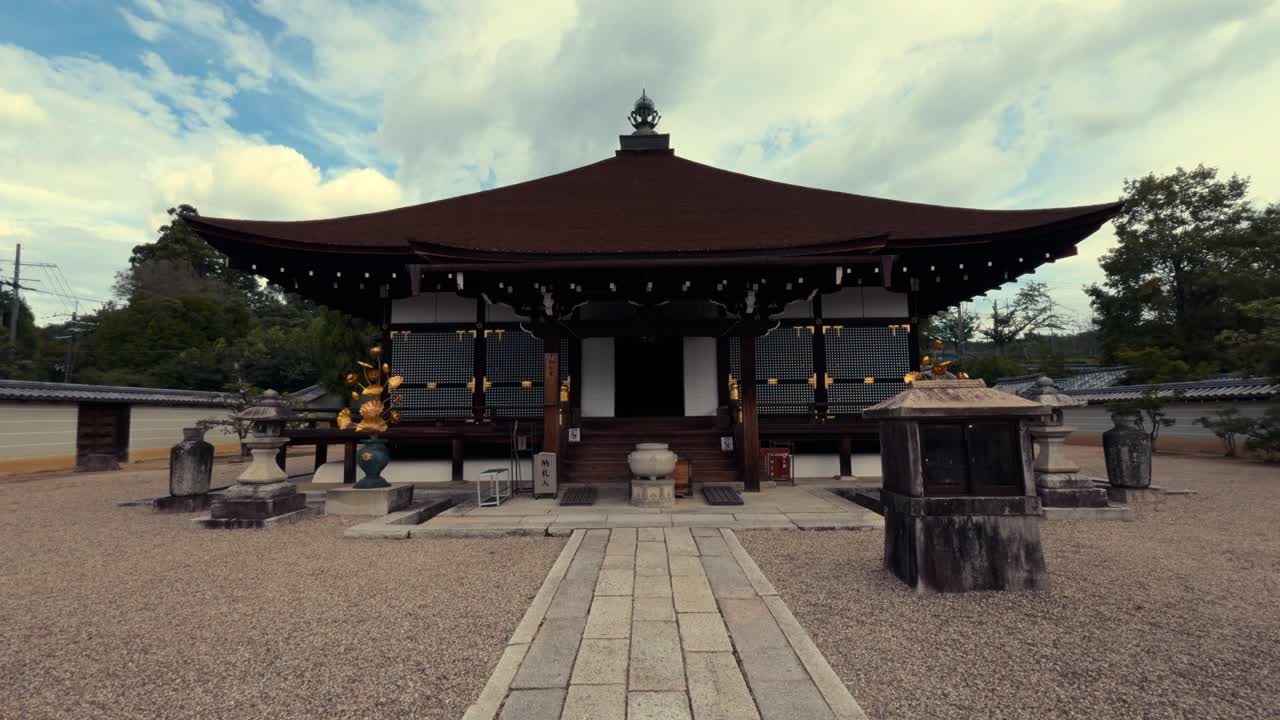 A serene Japanese temple with classic wooden architecture, stone lanterns, and a central walkway on a peaceful day with scattered clouds
