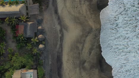 Mazunte-Beach-Birds-Eye-View-in-Oaxaca,-Mexico-With-Waves-Crashing-into-Shore-and-Thatched-Roofs-on-Land