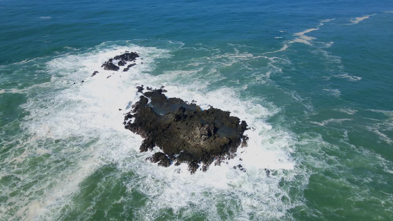 Veduta aerea dall'alto che mostra la schiuma delle onde che si infrangono contro una roccia corallina sotto la luce del sole.