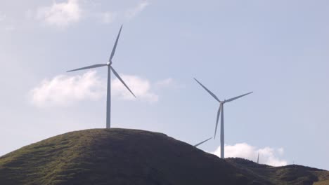 two wind turbines spinning on a hill in new zealand