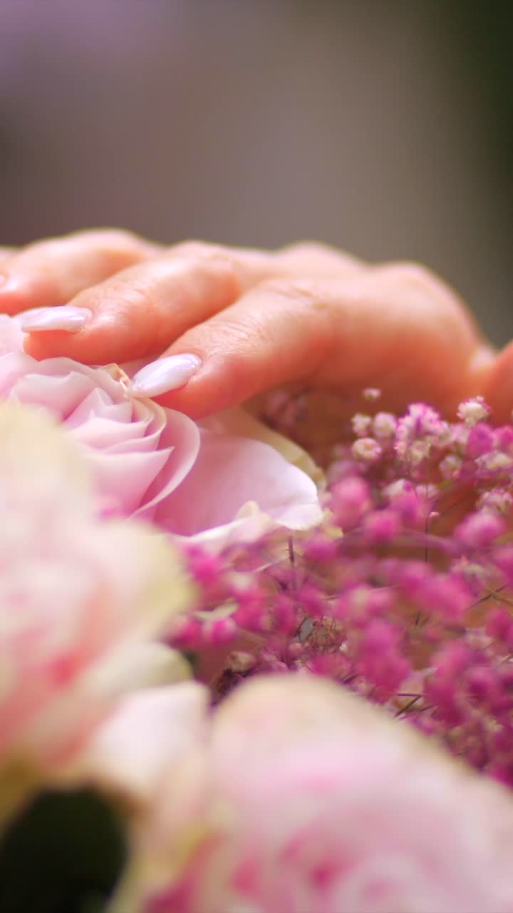 Mano femminile che accarezza delicatamente i fiori di un bouquet nuziale, primo piano verticale, profondità di campo ridotta.