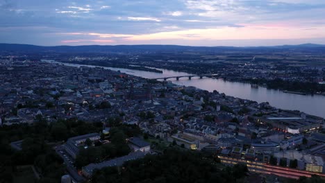 approaching aerial drone shot of mainz at magic hour night towards city center with with the cathedral and the dark rhine river water in the background showing a colorful sky