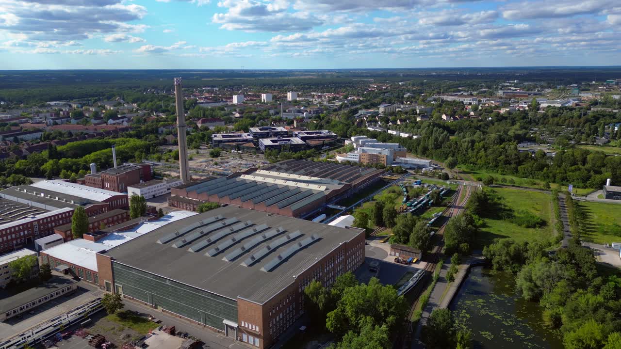 industrial buildings and a chimney in Hennigsdorf, Germany, with a train passing by. Fantastic aerial view flight fly reverse drone