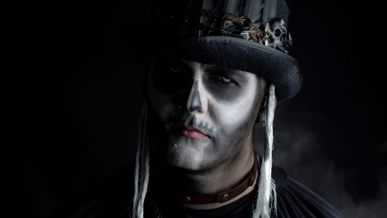 Sinister man with horrible Halloween skeleton makeup appearing from darkness when light falls on him