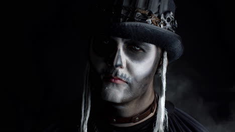 hombre siniestro con horrible maquillaje de esqueleto de halloween que aparece de la oscuridad cuando la luz cae sobre él