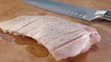 deslizador cercano disparado en cámara lenta de sal de molienda en una carne de cerdo cruda en un tablero de cortar de madera