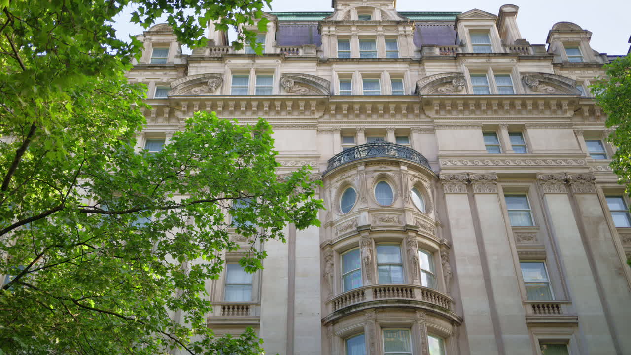 Green trees over an ornate historical building facade in London, England in daylight