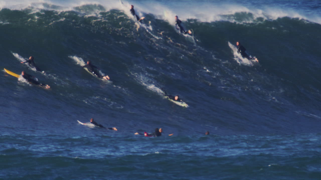 Slow motion view of surfers in lineup paddling to make it over the top as solo adventurer paddles to drop in on monster