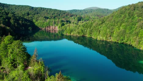 Aerial-View-Of-Tranquil-Lake,-Green-Forest,-And-Waterfall-In-Summer