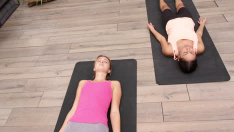 practicing yoga, two women lying on yoga mats in relaxation pose