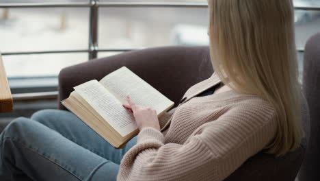 side view of a young lady reading a book, with her hand resting on the pages, she appears absorbed in her reading, creating a peaceful and reflective atmosphere in the cozy setting