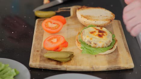 primer plano del montaje de una hamburguesa de pollo recién asada con mayonesa y pepinillos