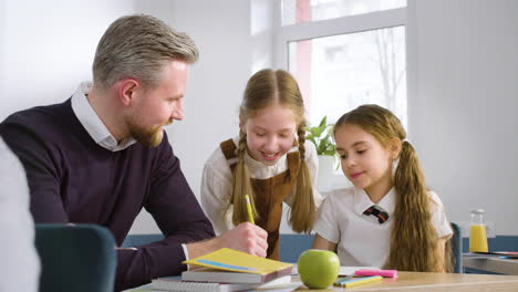 teacher sitting at desk resolving doubts to two female students in english classroom 2