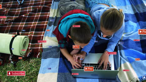 on blanket, children watching animation on laptop with play and subscribe buttons