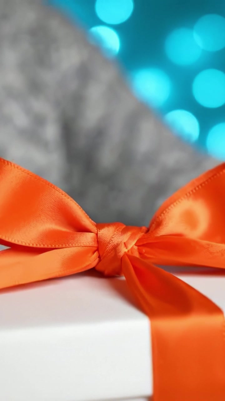 Un individuo che lega abilmente un elegante nastro arancione attorno a una confezione regalo su uno sfondo bokeh blu morbido e scintillante, mettendo in mostra creatività e premura.