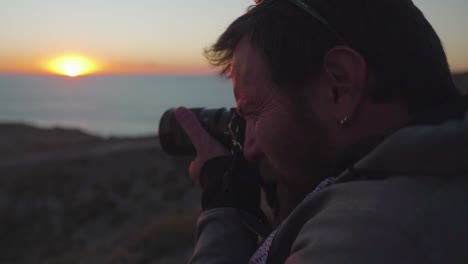 vista lateral de un hombre sosteniendo una cámara tomando fotos durante la puesta de sol - primer plano, tiro hacia atrás, cámara lenta