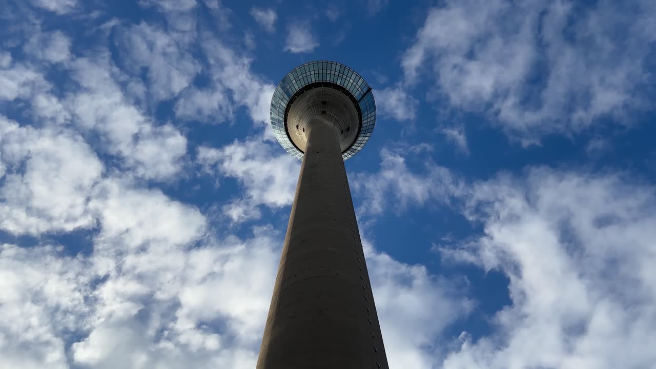 Low angle view of the iconic Rheinturm tower in Düsseldorf rising into a cloudy blue sky