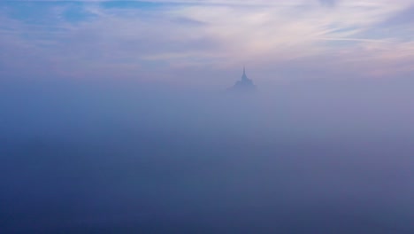 moody amazing aerial of mont saint-michel france rising out of the mist and fog in early morning