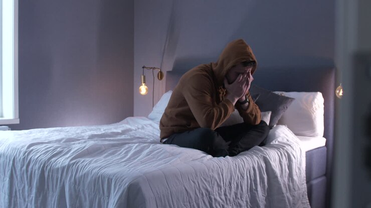 người đàn ông buồn ngồi trên giường với đôi chân chéo