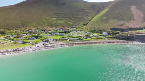 aerial drone flight in reverse over rosbeigh, ireland. revealing coastal village, open beach, and vast hillside under sunny skies. expansive rural scenery unfolds with motion.