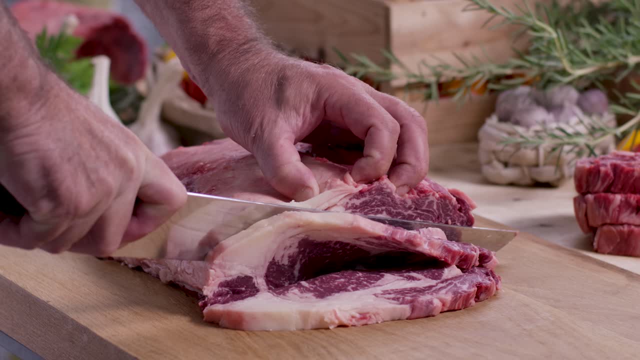 Primo piano di uno chef gourmet che taglia sapientemente una bistecca di ribeye marmorizzata da un grande arrosto di manzo crudo su un tagliere di legno nella cucina di casa