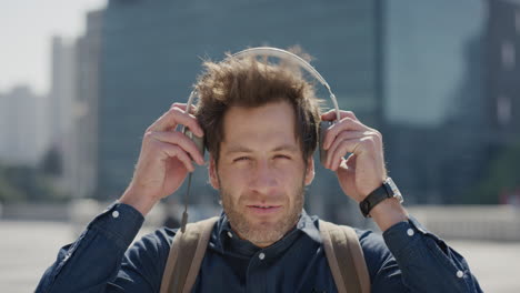 portrait attractive young businessman puts on headphones enjoying listening to music relaxing in sunny urban city wind blowing slow motion