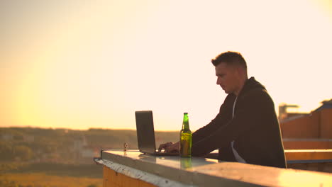 Hipster-man-with-a-laptop-on-the-edge-of-the-roof.-Freelancer-at-work.-Wireless-mobile-Internet.-He-works-on-the-Internet.