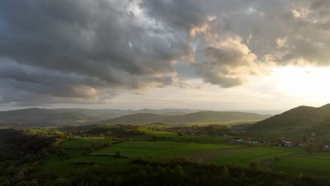 Cinematic-drone-captures-the-golden-evening-light-over-a-rural-countryside,-with-fields-and-trees-bathed-in-the-warm-glow-of-the-setting-sun