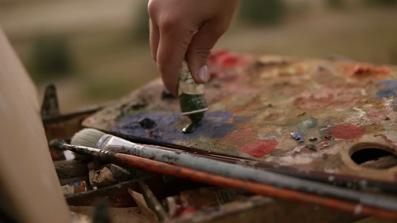 Art, creativity and people concept. Close up of artist extrudes paint from the tube on the palette outdoors