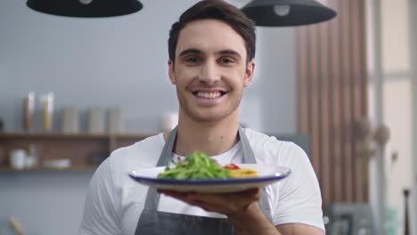 chef sonriente hombre sosteniendo un plato con ensalada en la cocina