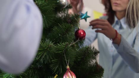 Close-Up-view-of-a-little-artificial-Christmas-tree-decorated-by-happy-smiling-office-workers.-Christmas-and-New-Year-celebration