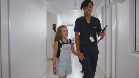 nurse walking holding hands with girl patient in busy hospital corridor