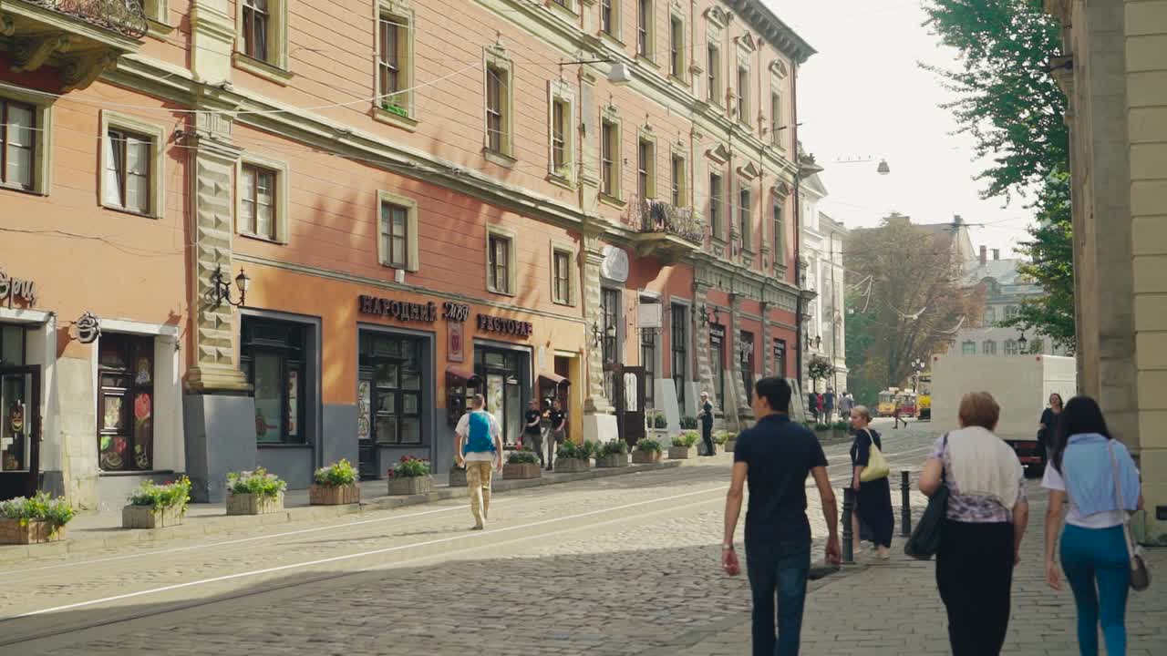 Central bygade med gamle bygninger og turister, der går på den. Folk går på den gamle brostensbelagte vej i den historiske by på en solrig sommerdag.