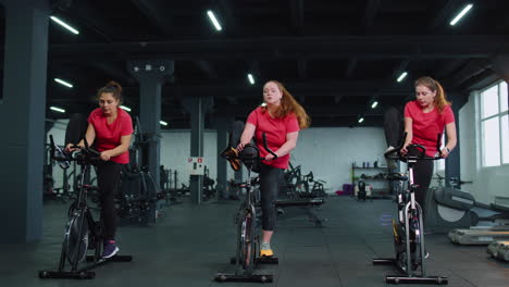 Grupo-De-Mujeres-Atléticas-Montando-En-Rutina-De-Entrenamiento-De-Bicicleta-Estacionaria-Giratoria-En-El-Gimnasio,-Pérdida-De-Peso-En-Interiores