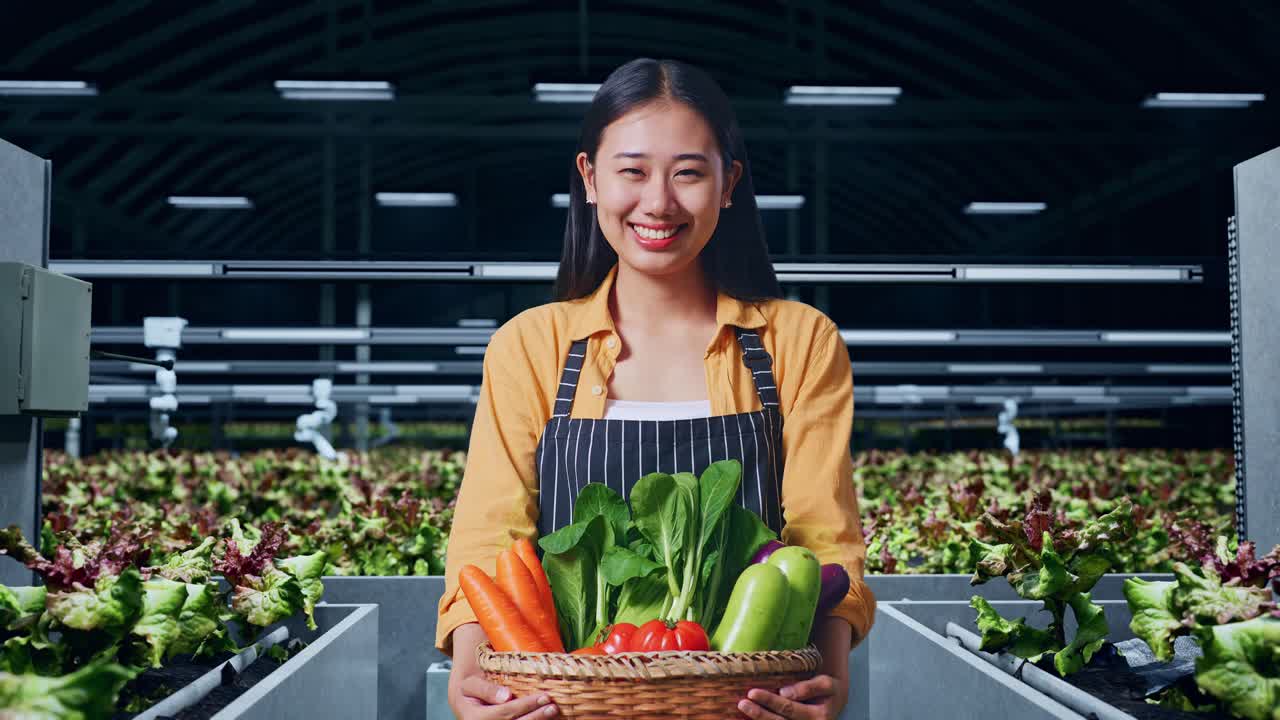 아시아 여성 농부 는 채소 바구니 를 들고 똑똑 한 농장 에서 따뜻 한 미소 를 짓고 있다