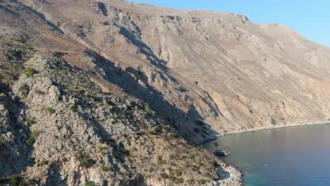 Drone-view-in-Greece-flying-a-brown-hill-on-a-mountain-next-to-the-blue-sea-of-the-mediterranean-on-a-sunny-day