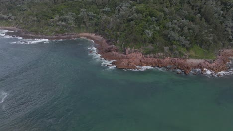 Las-Olas-Del-Océano-Salpican-En-La-Costa-Rocosa-Del-Monte-Yacaaba-Con-Bosque-Verde---Cabeza-De-Yacaaba-En-Nido-De-Halcones,-Nsw,-Australia