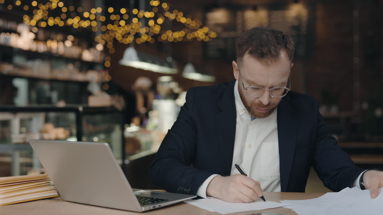 Uomo che lavora con laptop e documenti in un bar