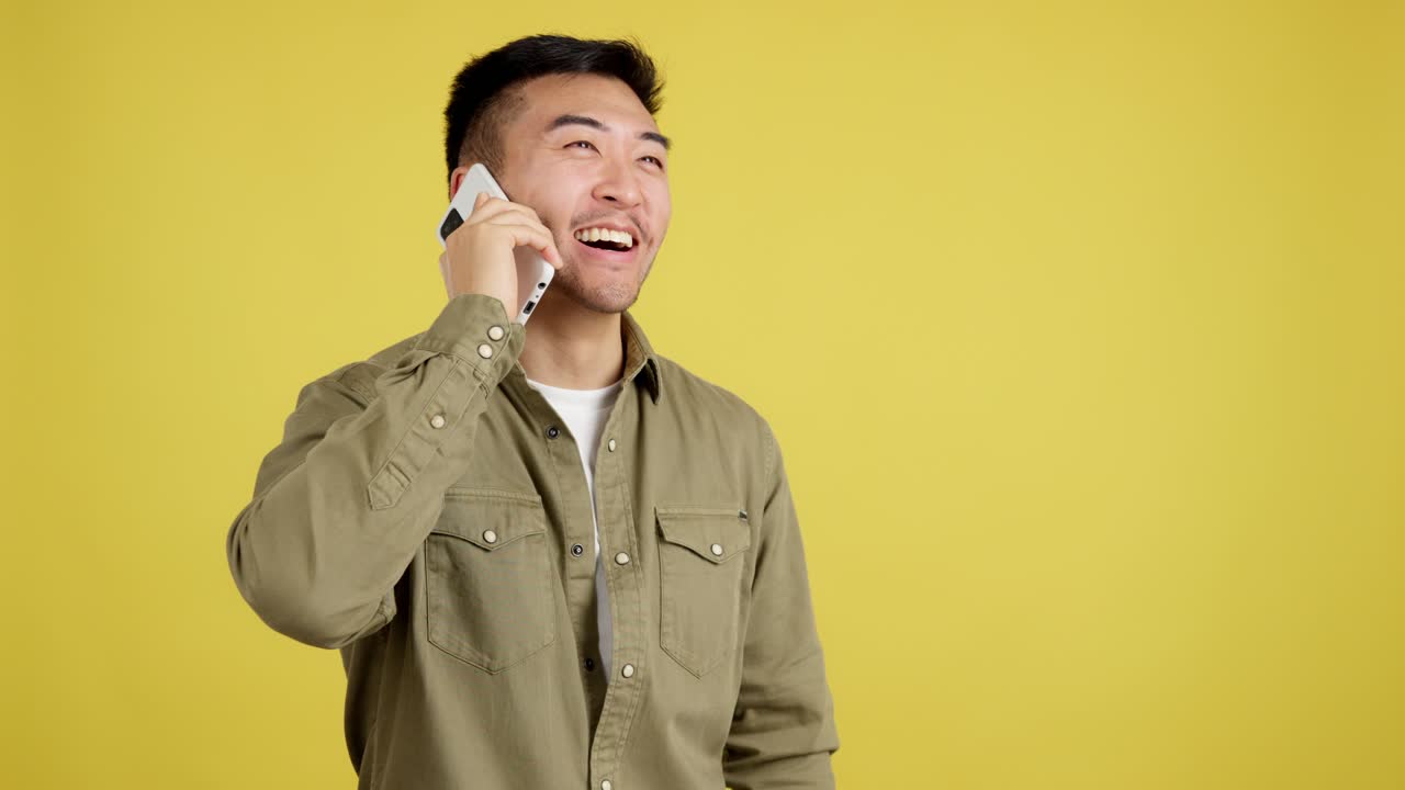 Young Asian man talking on a mobile phone against a yellow background, showing various happy expressions.