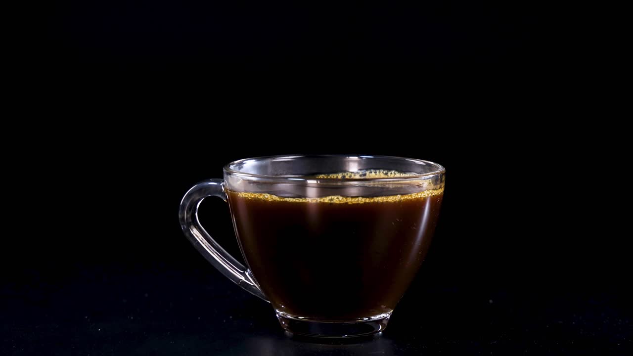 A sugar cube drops into a coffee cup, creating a splash against a dark background