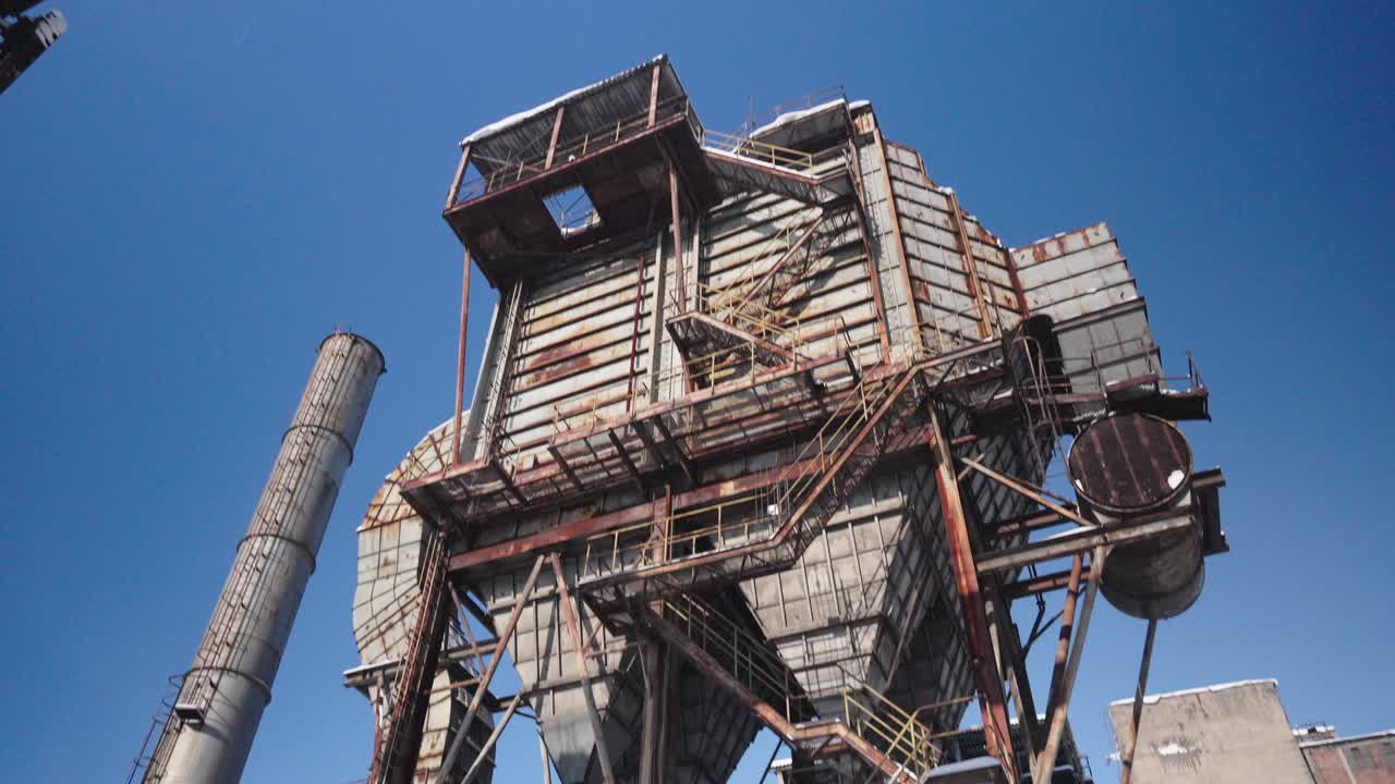 An old, rusted and dilapidated former electrostatic precipitator with a towering chimney under a clear winter blue sky