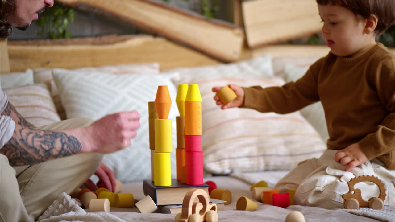 Father playing with his son with colourful, ecological wooden toys on the bed