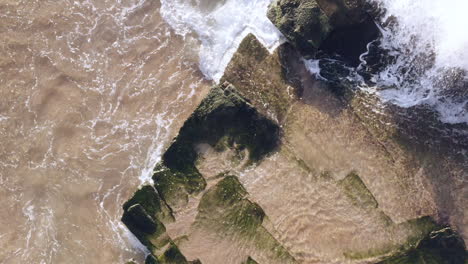 white waves rolling up onto seaweed covered horizontal bedded sedimentary ocean rocks aerial view panning from bottom of screen turimetta beach sydney australia